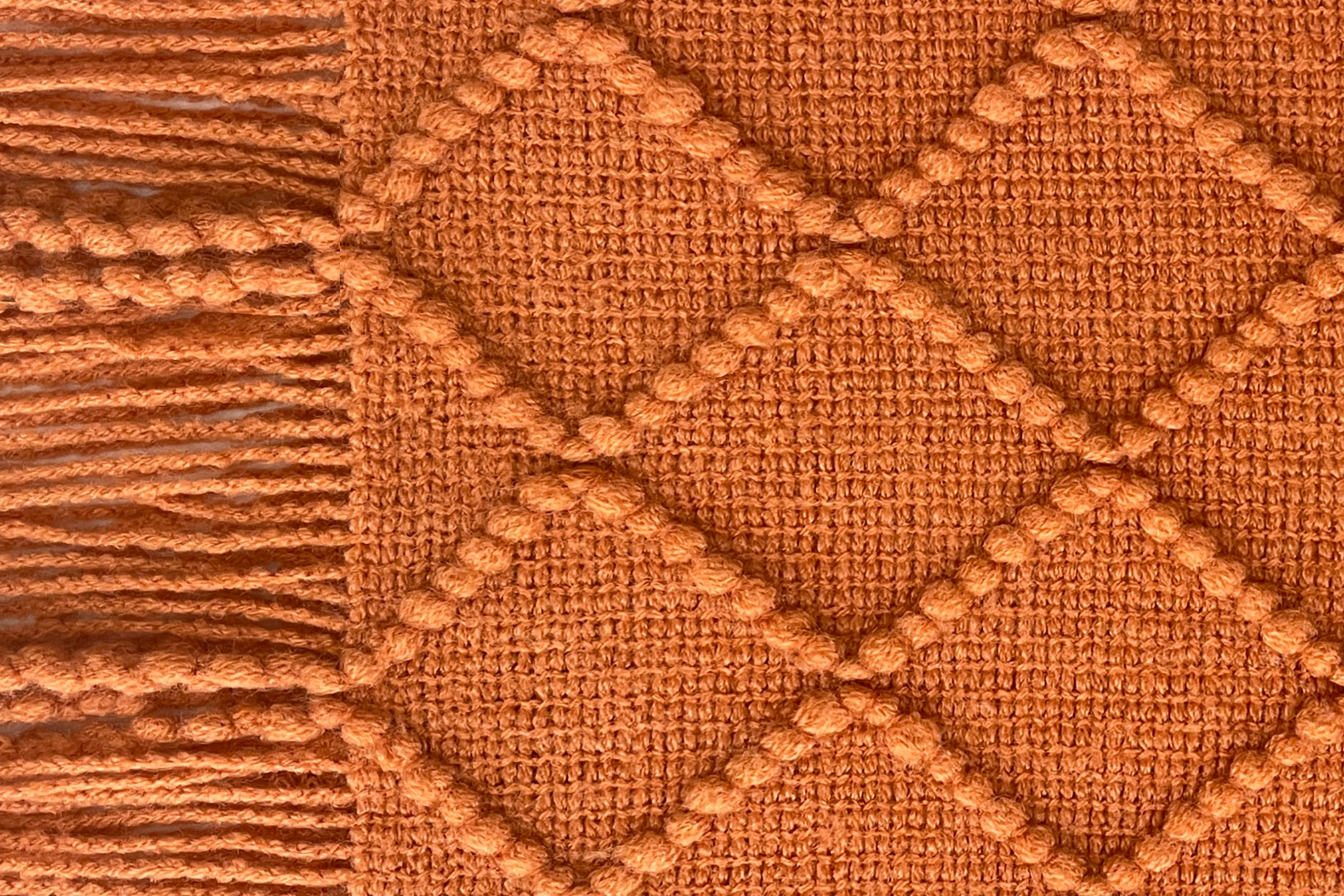 Close-up of a woolen heated sofa blanket with tassels in the colour red earth with a geometric pattern