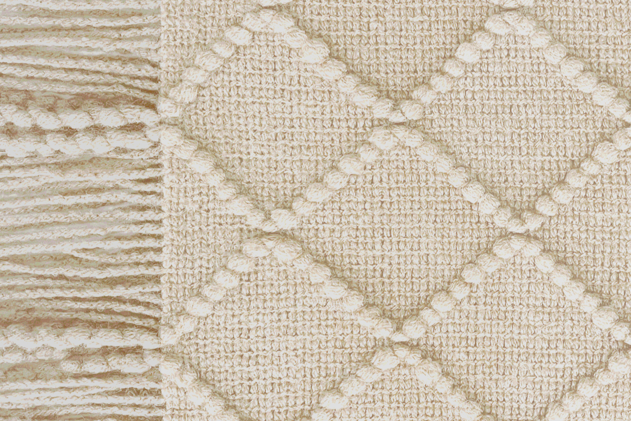 Close-up of a woolen heated sofa blanket with tassels in the colour white clay with a geometric pattern