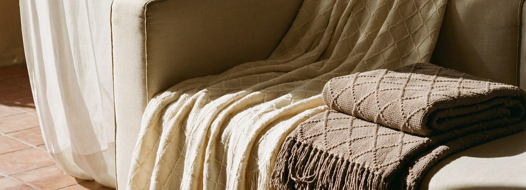 White Clay and Taupe Dawn BOHEM draped over a linen sofa in afternoon light
